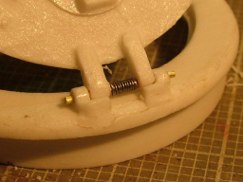 So I cut away the molded resin spring in the center section of the hinge pin. Then drilled out both the mount on the ring and the split hatch itself. Using .0315 (1/32nd inch) brass rod I made a new hinge pin. Once that was done I chucked another peice of the same size stock in my Dremel motor tool. I slowly rotated the chuck winding fine (.010) diameter steel thread around the brass rod. Then carefully removed the wound steel thread and slipped it over the brass hinge pin like a sleeve as it passed through the ring and corresponding hatch hinge holes.